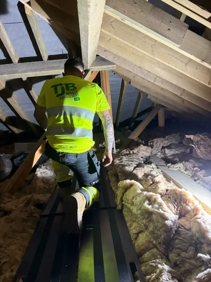 TJB team member in branded hi-vis clearing old insulation from a loft