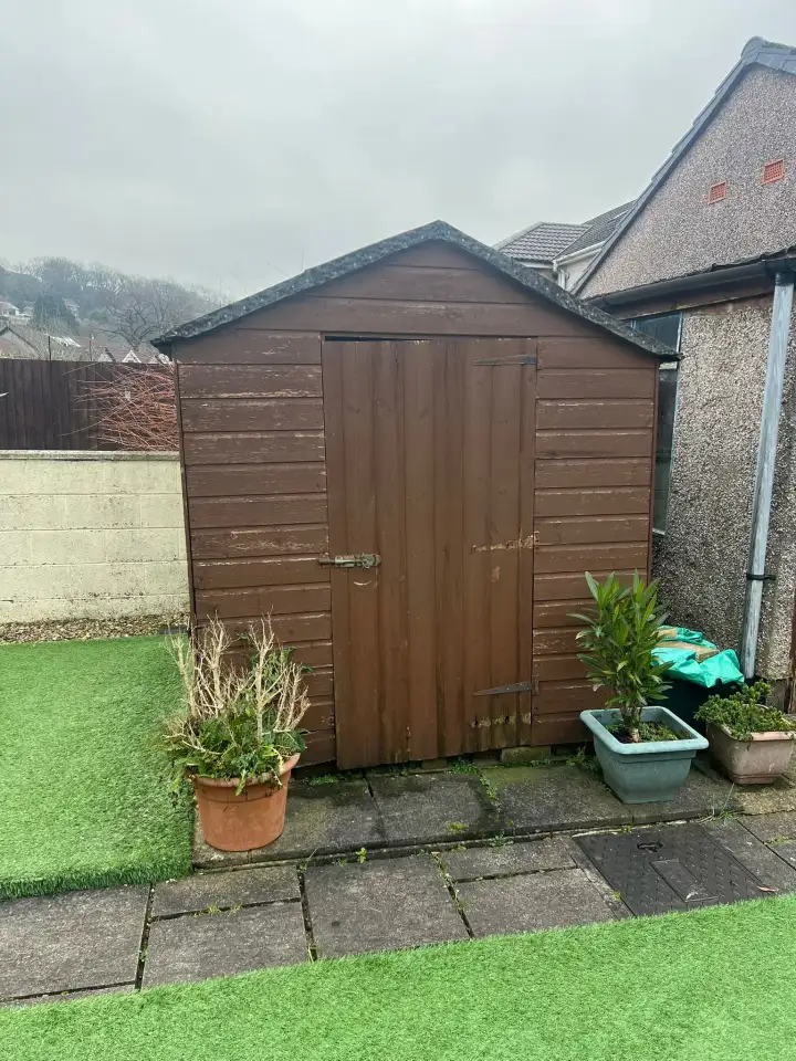Brown timber garden shed on a patio before removal