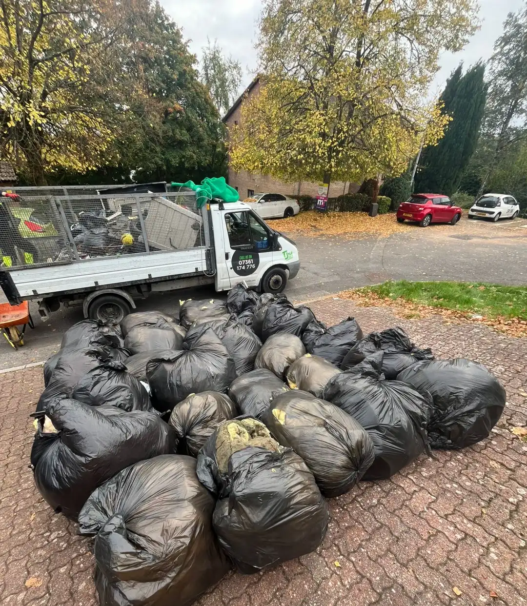 TJB Waste Management tipper truck beside bagged waste ready for removal from a driveway